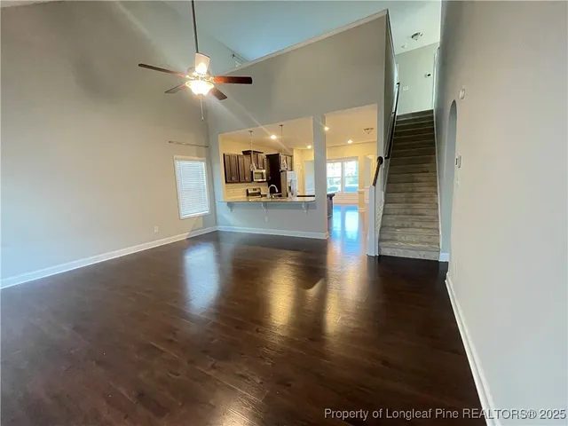 an empty room with wooden floor a ceiling fan and kitchen view