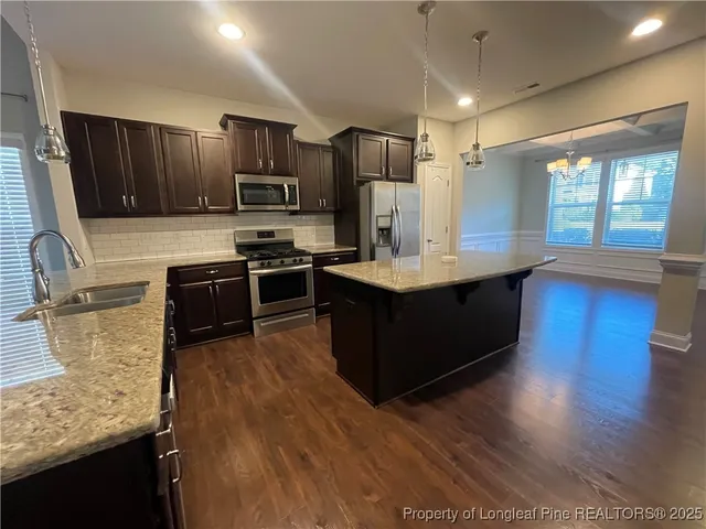 a kitchen with stainless steel appliances kitchen island granite countertop a sink stove refrigerator and microwave