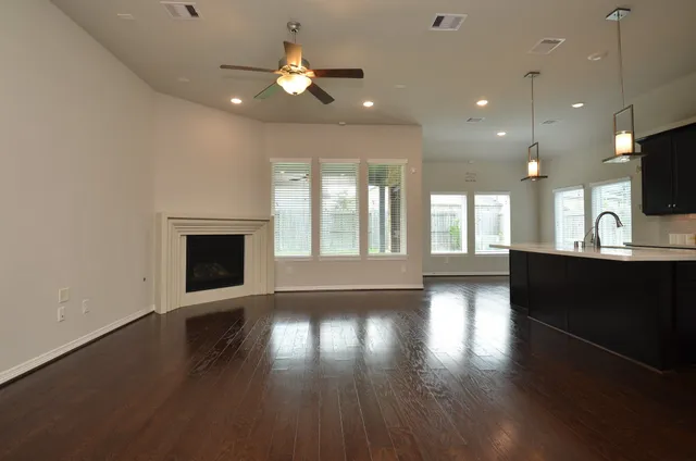 a view of an empty room with wooden floor and a kitchen