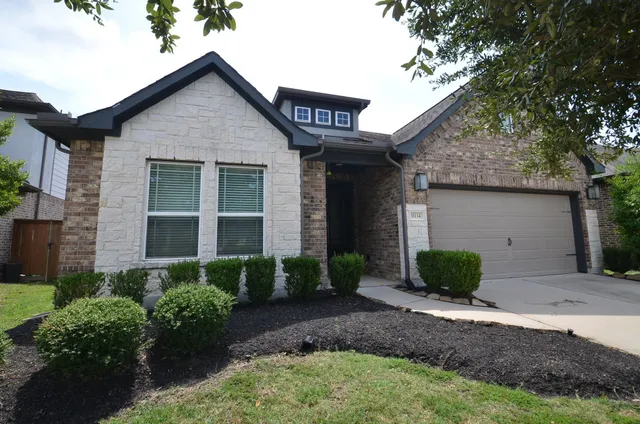 a view of a brick house with many windows plants and large tree