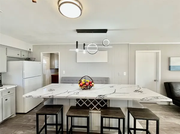 a large white kitchen with a stove a sink a refrigerator and dining table with wooden floor