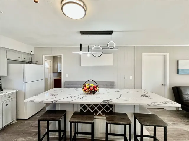 a large white kitchen with a stove a sink a refrigerator and dining table with wooden floor