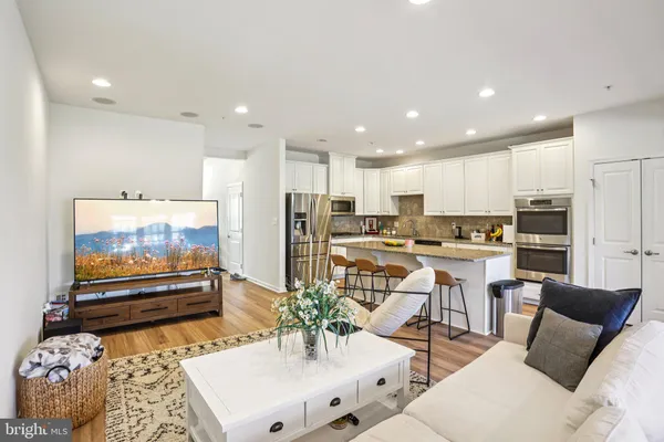 a living room with stainless steel appliances furniture a rug and a kitchen