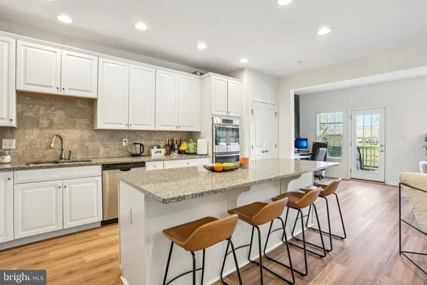a kitchen with stainless steel appliances granite countertop a stove top oven a sink a refrigerator with white cabinets and wooden floor