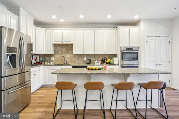 a kitchen with stainless steel appliances granite countertop a stove top oven a refrigerator a sink and white cabinets with wooden chairs