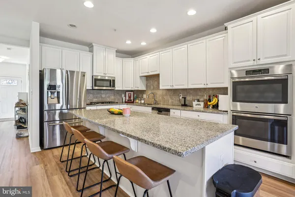 a kitchen with stainless steel appliances granite countertop a stove top oven a refrigerator a sink and white cabinets with wooden floor