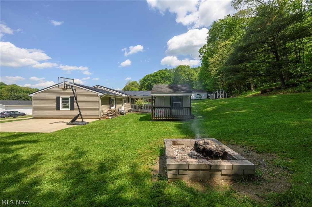 6105 Wolf Run Road Southeast Dennison, OH 44621 - Photo 6 of 35 Expansive green lawn featuring a stone fire pit, bordered by a wooded hillside
