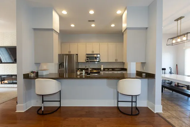 a living room with stainless steel appliances furniture a rug and a kitchen view