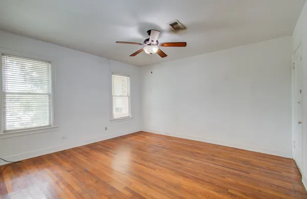 an empty room with wooden floor ceiling fan and windows