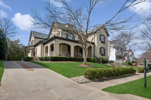 a view of a white house next to a yard with big trees and plants