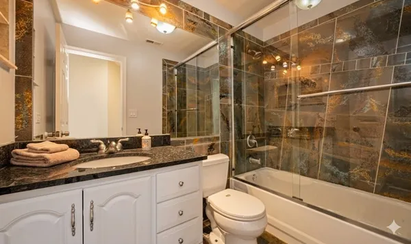 a bathroom with a granite countertop sink a toilet a mirror and shower