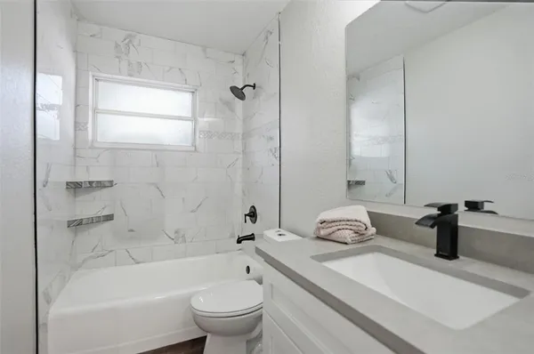 a bathroom with a granite countertop bathtub shower sink vanity mirror and toilet