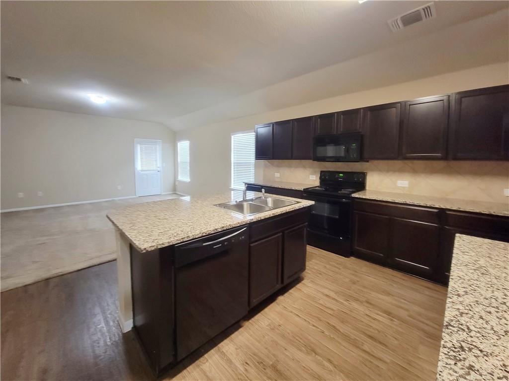 11924 Riparian Road Manor, TX 78653 - Photo 14 of 14 Kitchen with black appliances, an island with sink, open floor plan, backsplash, and dark brown cabinetry