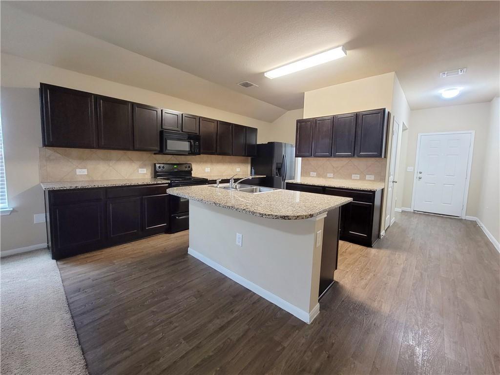 11924 Riparian Road Manor, TX 78653 - Photo 5 of 14 Kitchen with black appliances, decorative backsplash, a center island with sink, lofted ceiling, and dark wood-type flooring