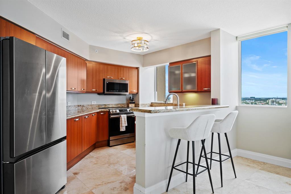 2011 North Ocean Boulevard, Unit 1605 Fort Lauderdale, FL 33305 - Photo 11 of 52 a kitchen with stainless steel appliances granite countertop a refrigerator a stove top oven a sink dishwasher and a refrigerator with wooden floor