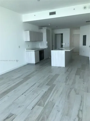 an empty room with wooden floor and kitchen view