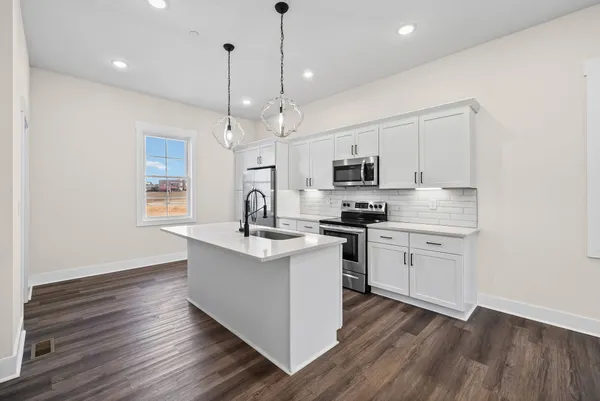 a kitchen with stainless steel appliances granite countertop a sink a stove a microwave oven a refrigerator with white cabinets and wooden floor