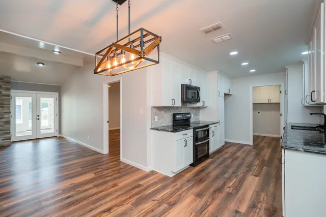 a kitchen with stainless steel appliances granite countertop a refrigerator a stove oven a sink dishwasher and white cabinets with wooden floor