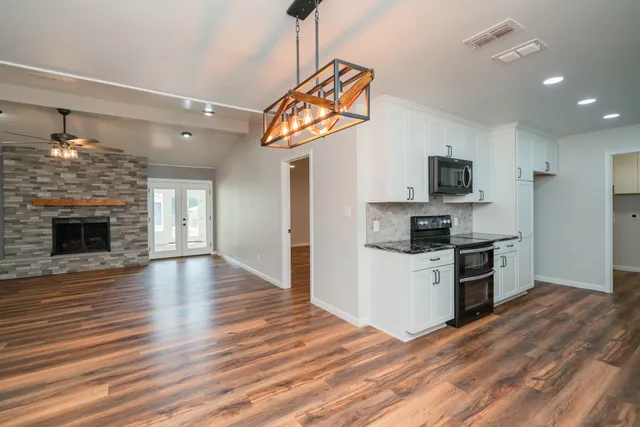 a kitchen with granite countertop a stove top oven a sink dishwasher a refrigerator and a fireplace with wooden floor