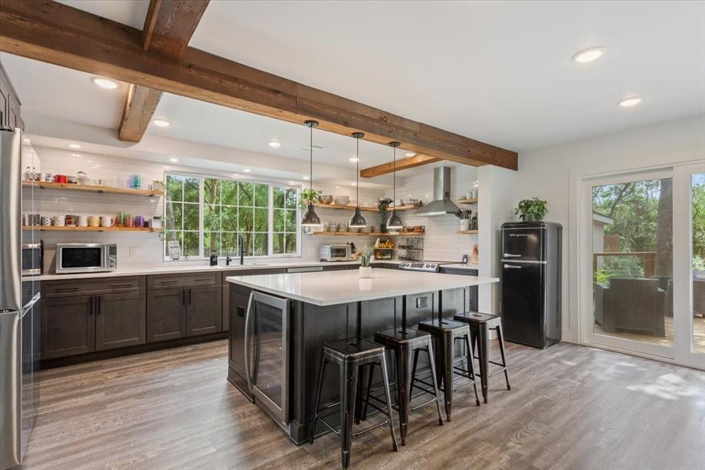 15988 Wortham Bend Road China Spring, TX 76633 - Photo 11 of 40 Kitchen featuring a large central island with seating, exposed wood beams, wood-finish flooring, a full-height tile backsplash, and a sliding glass door to an outdoor area