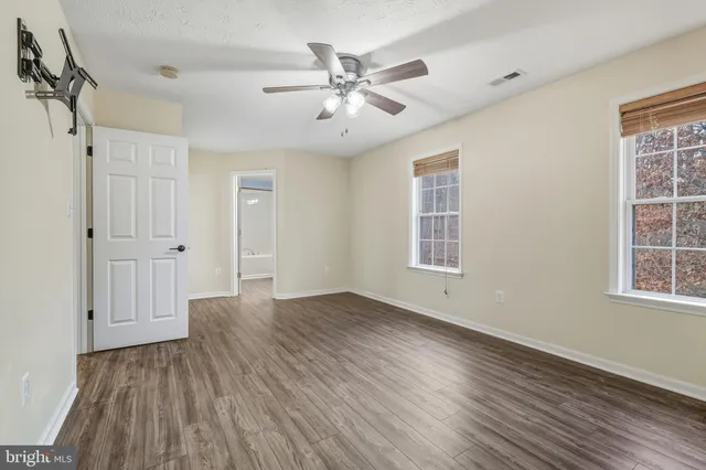 an empty room with wooden floor ceiling fan and windows