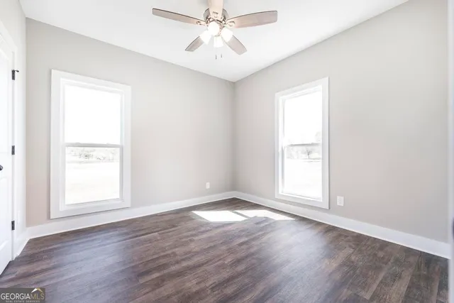 an empty room with wooden floor chandelier fan and windows