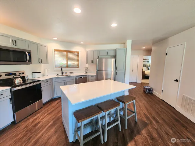 a large kitchen with stainless steel appliances kitchen island granite countertop a stove a sink a refrigerator and white cabinets with wooden floor