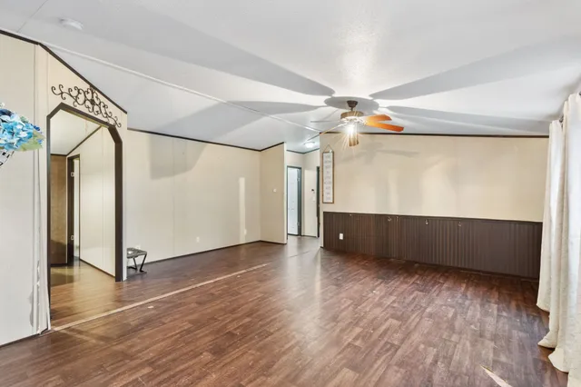 a view of an empty room with wooden floor and a ceiling fan