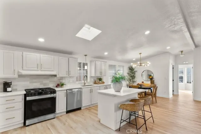 a kitchen with stainless steel appliances kitchen island granite countertop a stove a sink a refrigerator and white cabinets with wooden floor