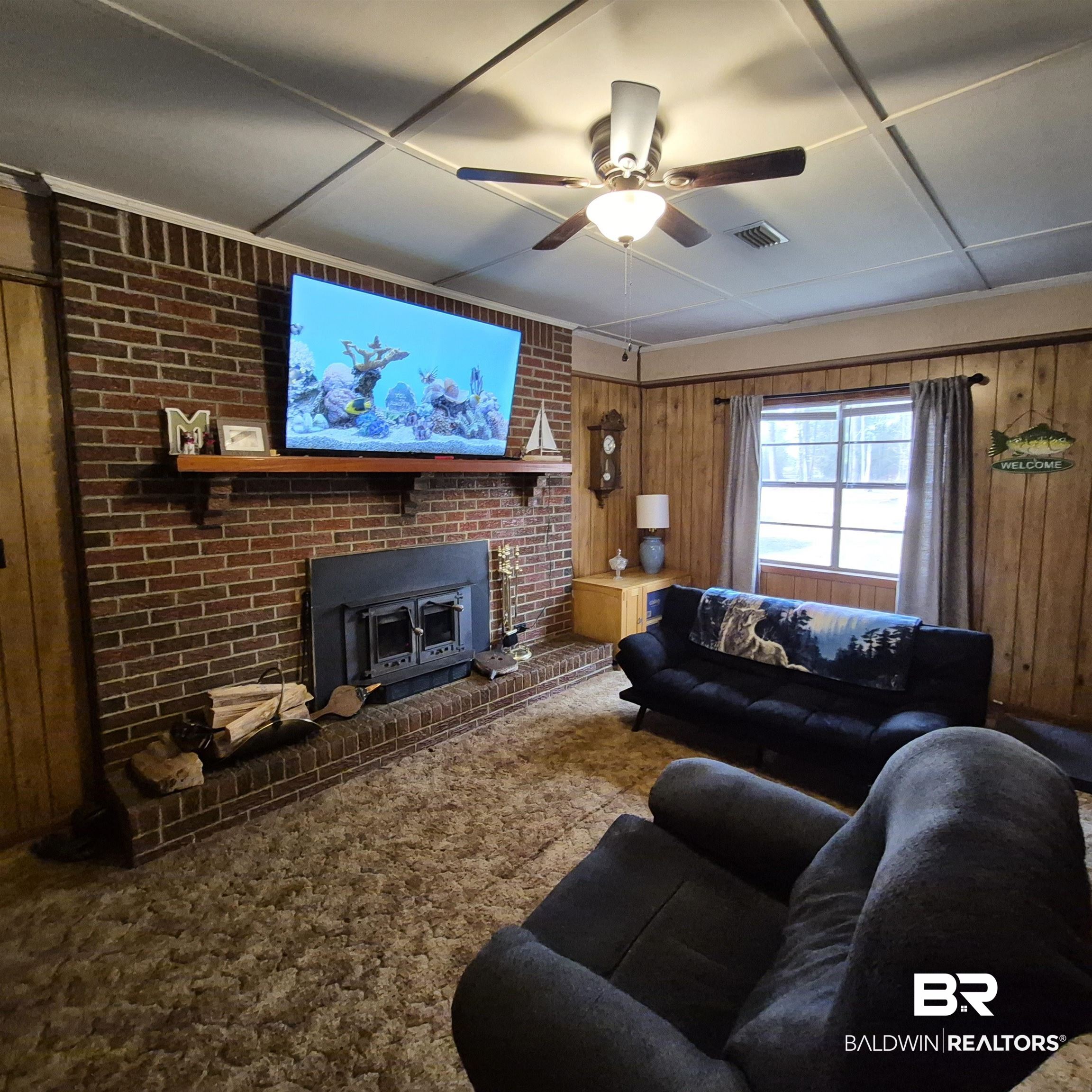 491 Forrest Avenue Castleberry, AL 36432 - Photo 11 of 33 Carpeted living room featuring wooden walls, a fireplace, and ceiling fan