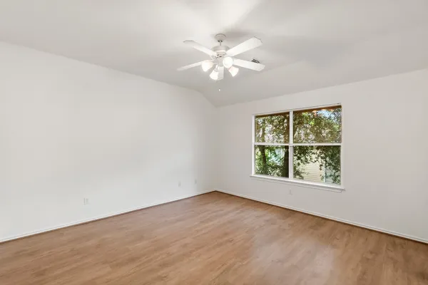an empty room with wooden floor chandelier fan and windows