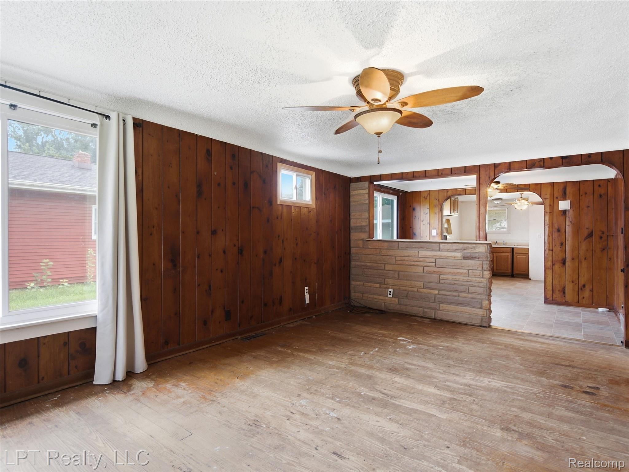 Wood-panelled walls, ceiling fan with light fixture, multiple windows, stone-faced half wall, arched doorways
