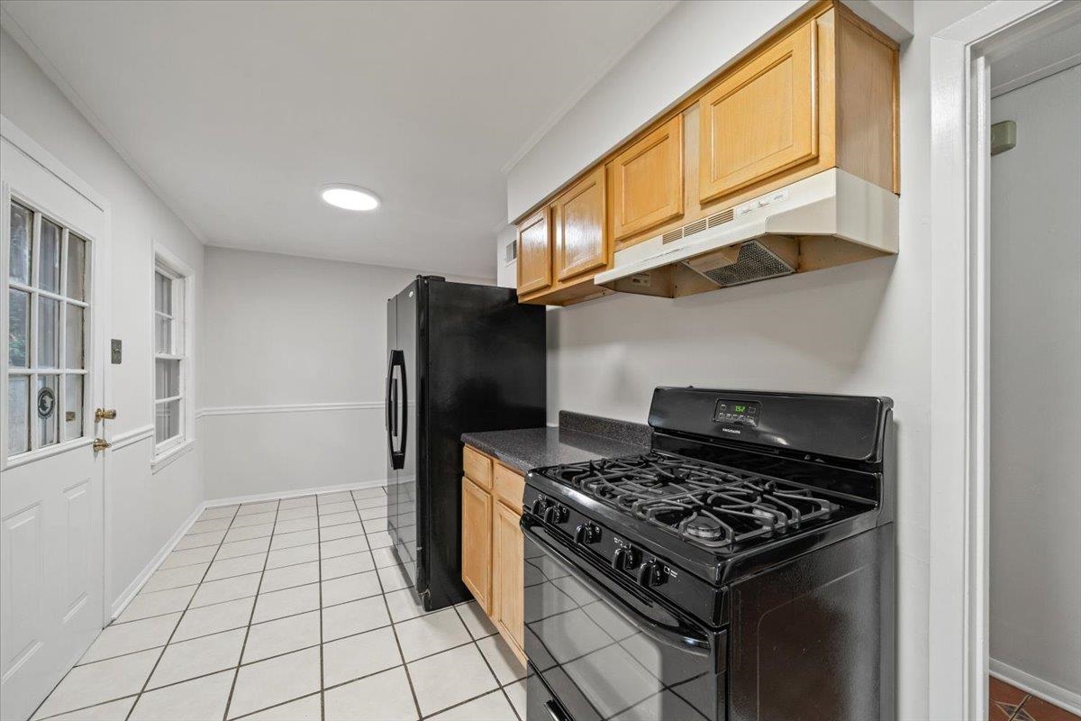 1554 Hopewell Road Memphis, TN 38117 - Photo 14 of 24 Kitchen with black appliances, dark countertops, under cabinet range hood, light tile patterned floors, and light brown cabinetry