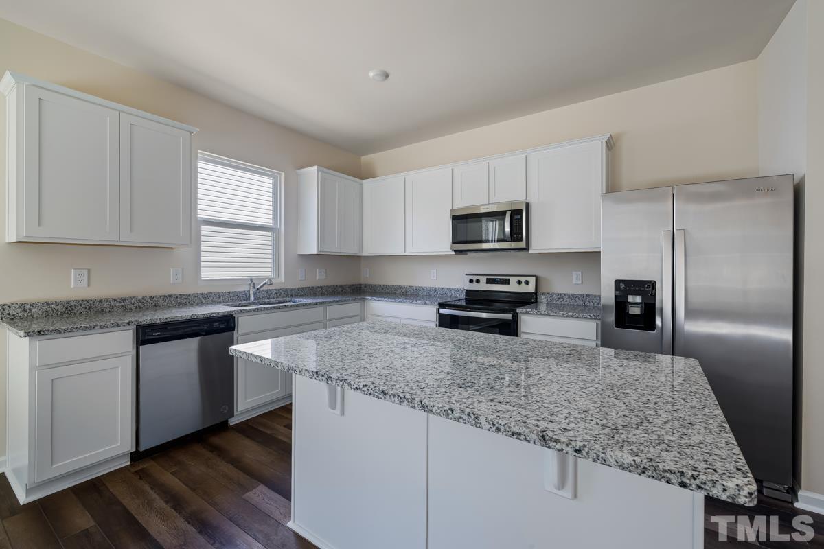 a kitchen with granite countertop a sink a counter top space cabinets stainless steel appliances and a window