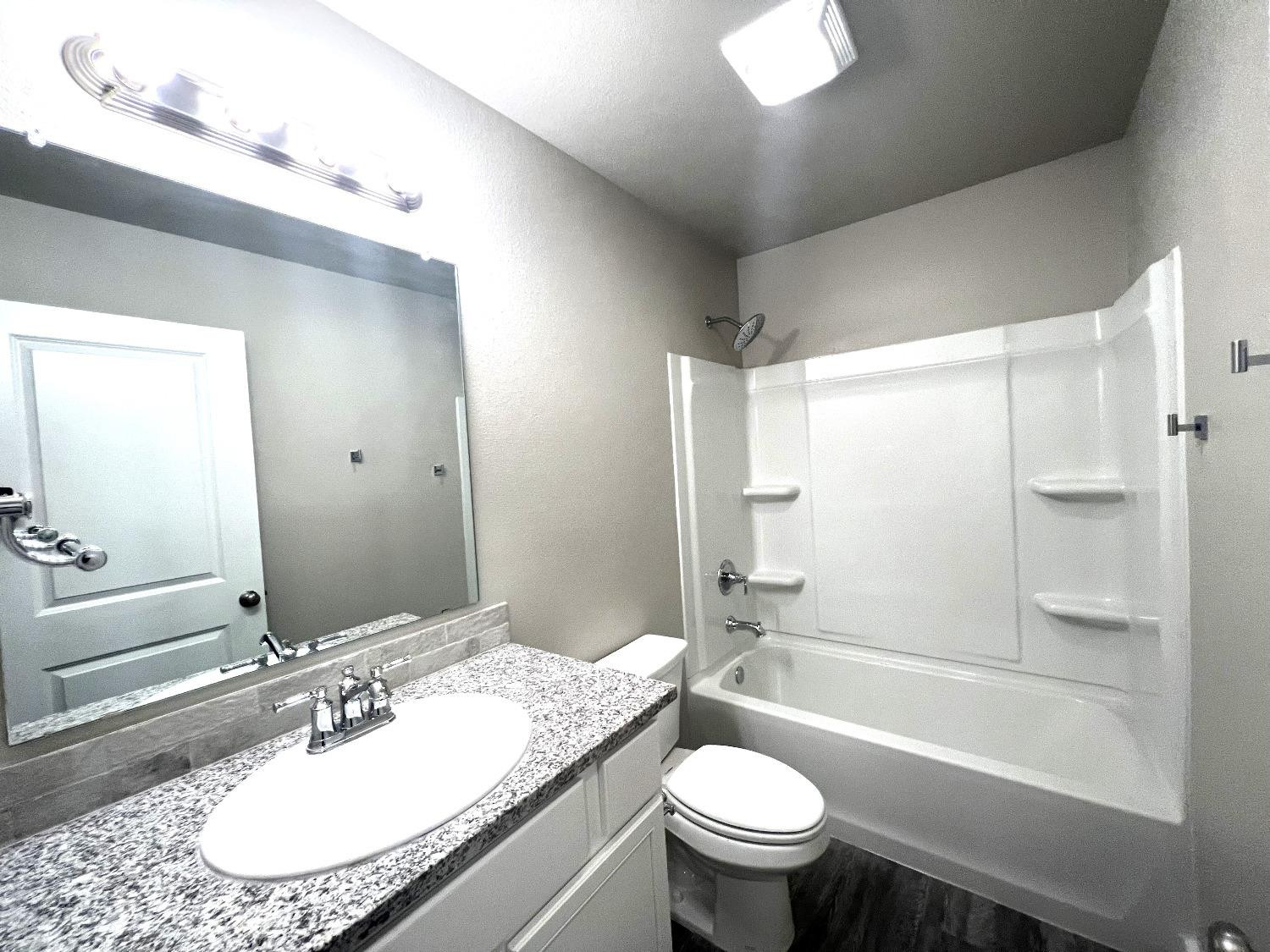 13705 Avenue Q Lubbock, TX 79423 - Photo 7 of 13 a bathroom with a granite countertop sink toilet mirror and bathtub