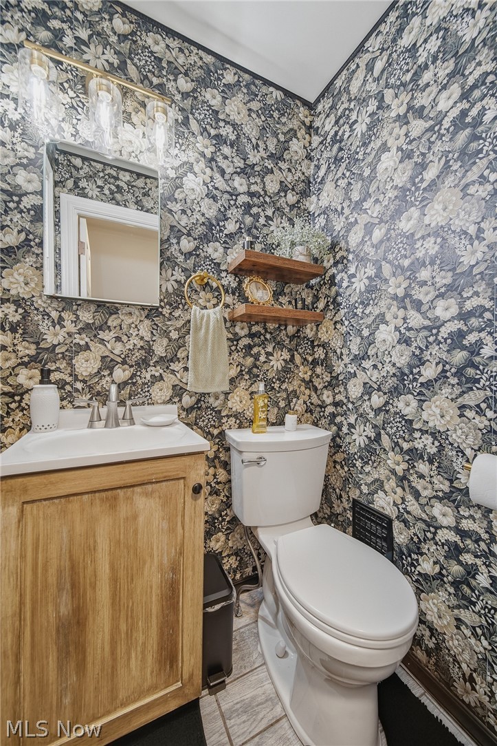 2231 Brockway Road University Heights, OH 44118 - Photo 15 of 46 Powder room featuring a floral patterned wallpaper, a single-sink vanity with a light wood-finish cabinet, a rectangular mirror, and a gold-finish four-bulb vanity light fixture