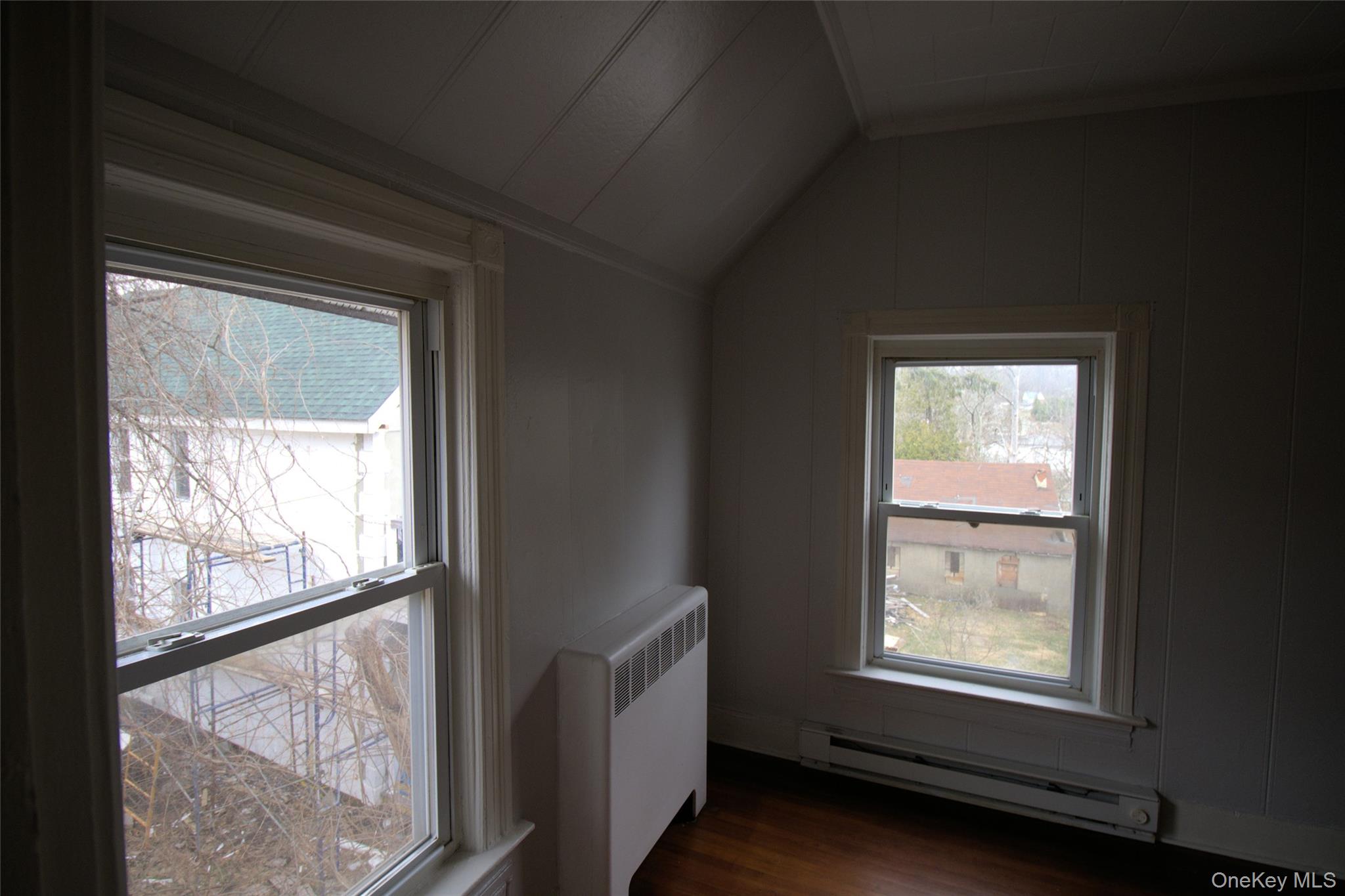 9 Spring Street Liberty, NY 12754 - Photo 11 of 29 Room featuring two double-hung windows with white trim, wood-finish flooring, white paneling, and a painted radiator