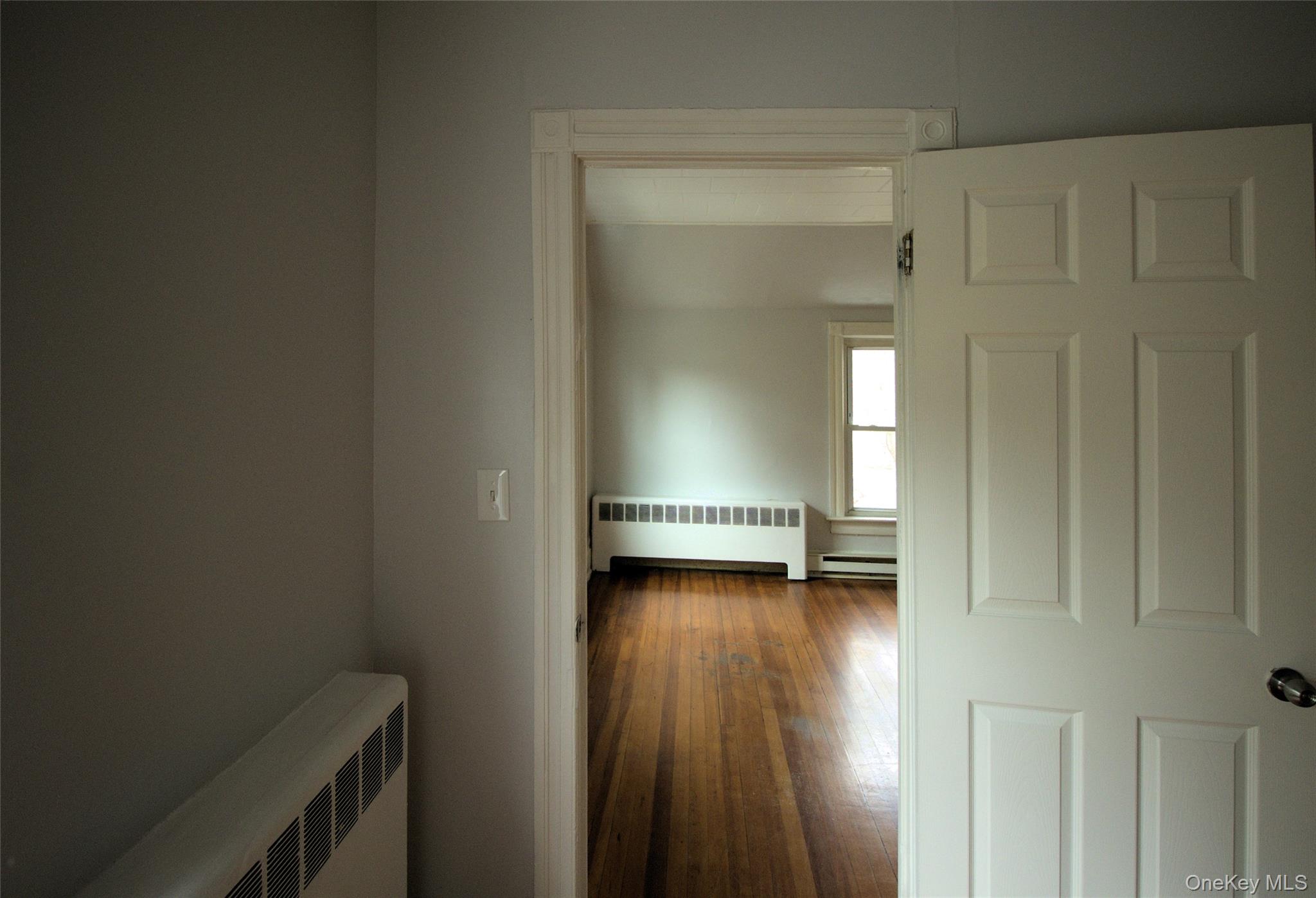 9 Spring Street Liberty, NY 12754 - Photo 13 of 29 Room entry featuring a paneled interior door, painted trim, light gray walls, and hardwood flooring extending into the room beyond