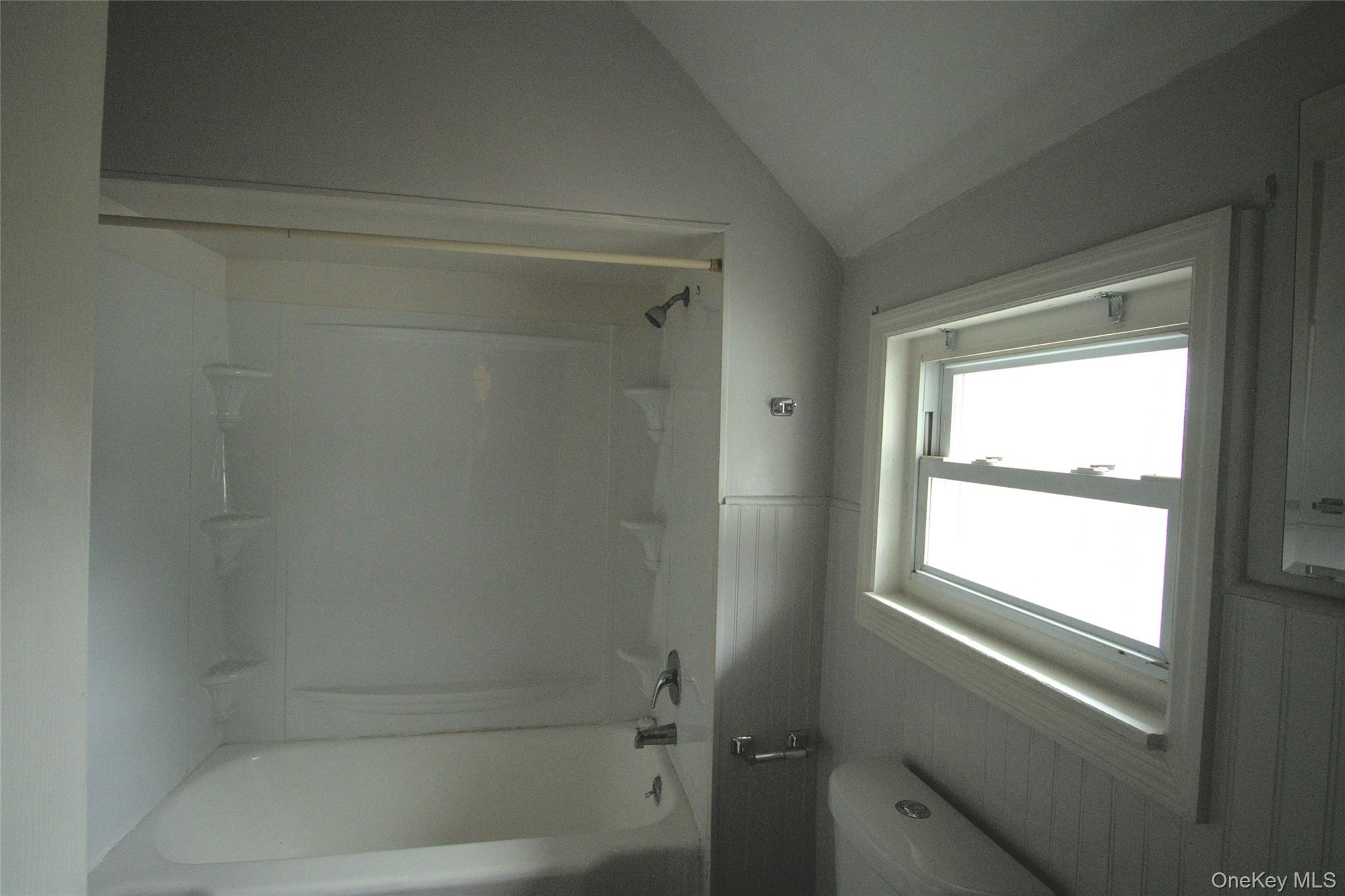 9 Spring Street Liberty, NY 12754 - Photo 7 of 29 Bathtub and shower combination with white surround, featuring a single window with white trim, and white wainscoting