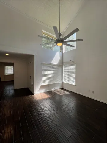 a view of an empty room with wooden floor and a ceiling fan