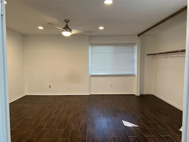 an empty room with wooden floor a ceiling fan and windows