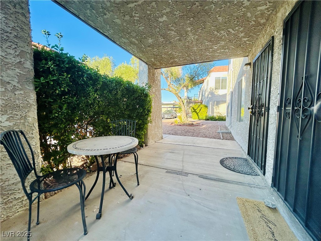 524 Fir Street, Unit 203 Boulder City, NV 89005 - Photo 6 of 7 This inviting patio under a covered walkway, surrounded by lush greenery and offering a serene view of the well-maintained courtyard. The secure entrance with stylish black gates adds a touch of elegance and security to this charming outdoor space.