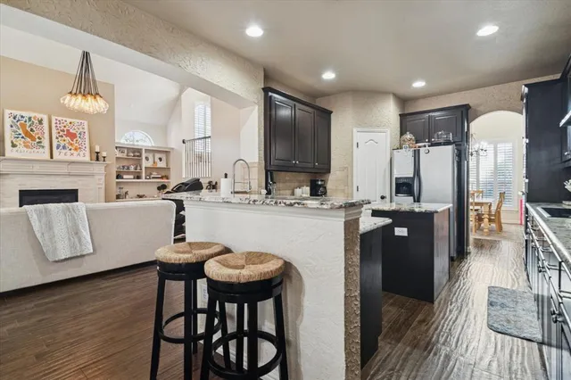 a kitchen with stainless steel appliances granite countertop a refrigerator a stove and a dining table with wooden floor