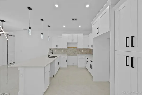 a large white kitchen with granite countertop a stove a sink a refrigerator and white cabinets with wooden floor