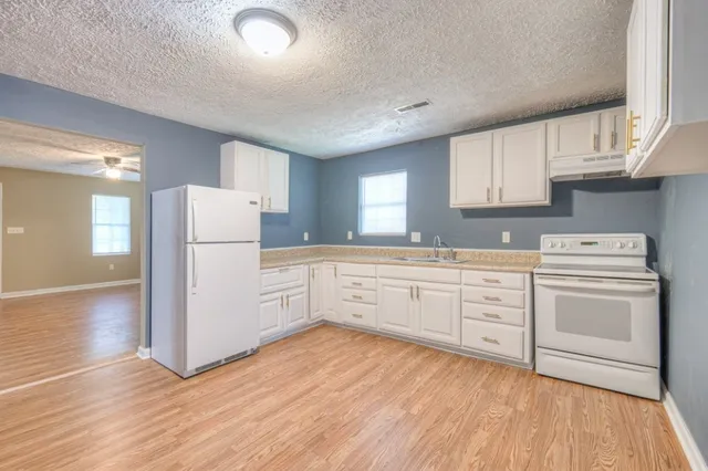 a kitchen with a white refrigerator oven a sink dishwasher and white cabinets with wooden floor
