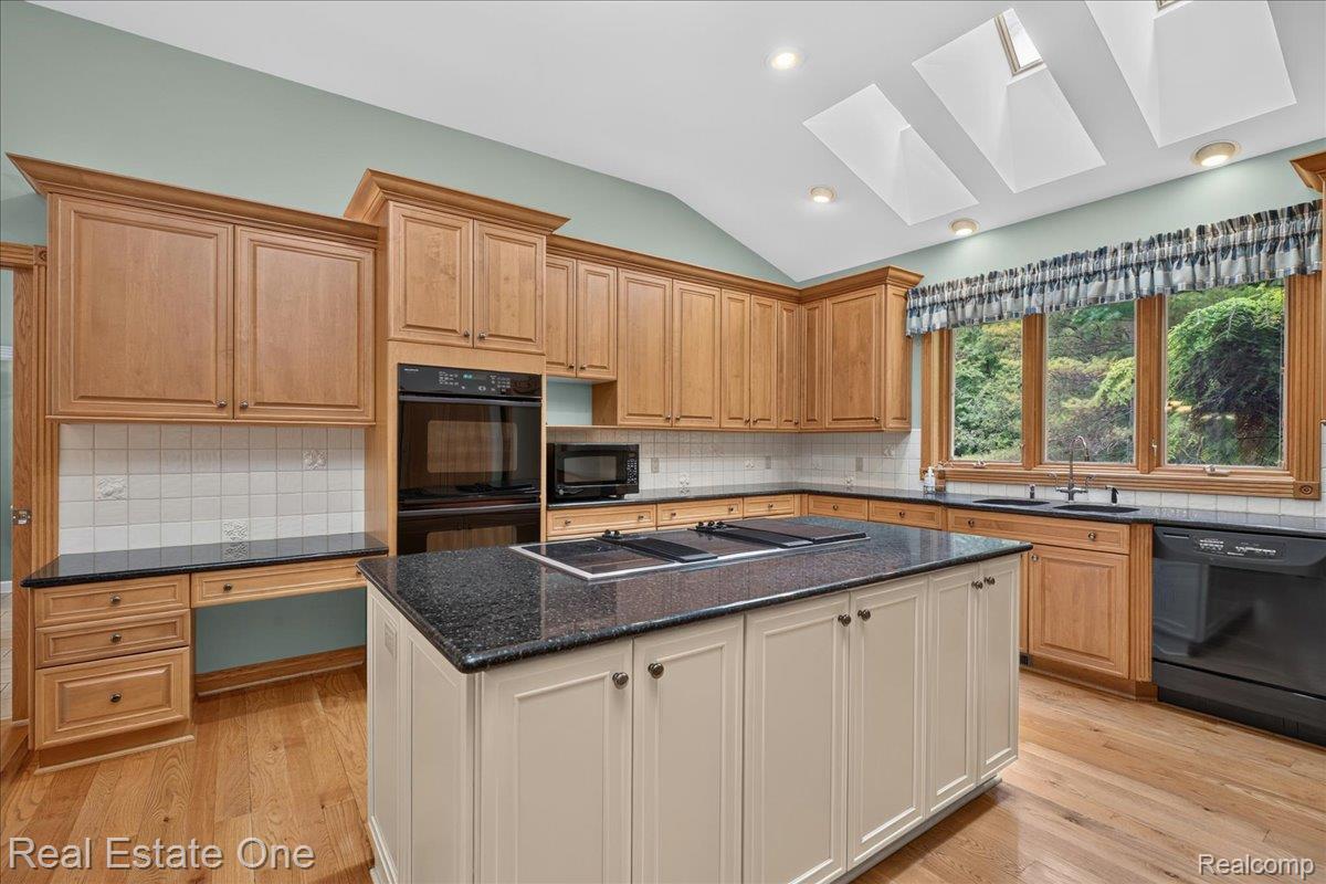 425 Courtney Road Leonard, MI 48367 - Photo 24 of 89 Kitchen featuring wood-finish flooring, an extensive island with a dark countertop, full-height cabinetry, integrated double ovens, and multiple skylights