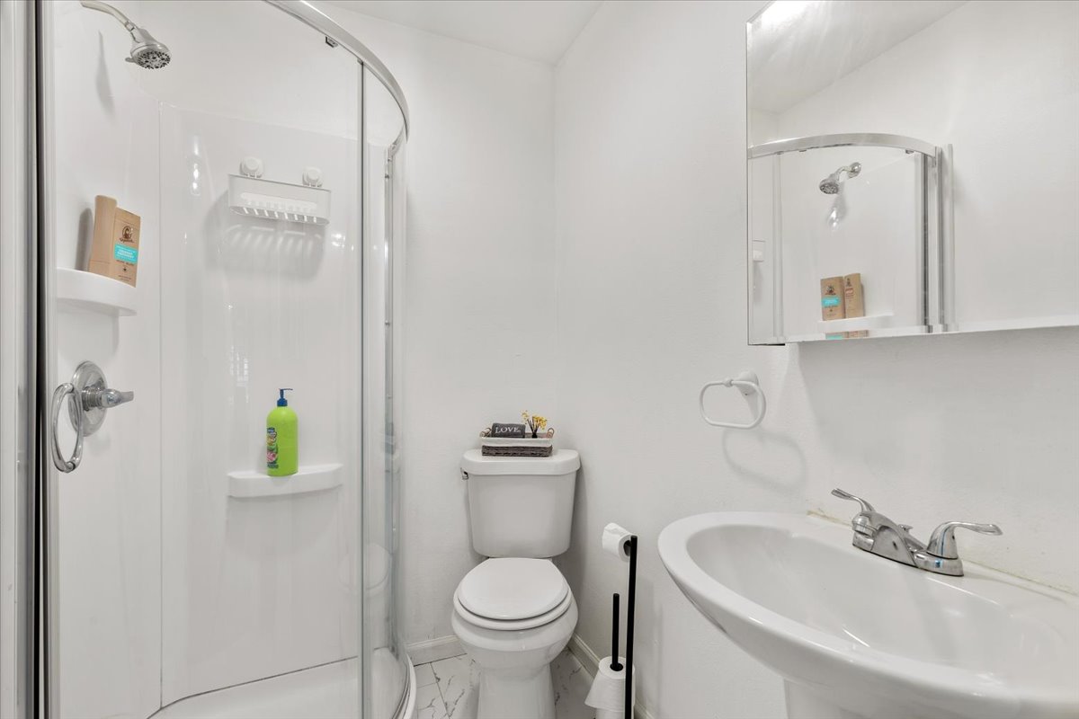 607 Short Street Smithville, TX 78957 - Photo 22 of 31 Compact bathroom featuring a curved glass shower enclosure, pedestal sink with chrome faucet, wall-mounted mirrored medicine cabinet, and a white toilet