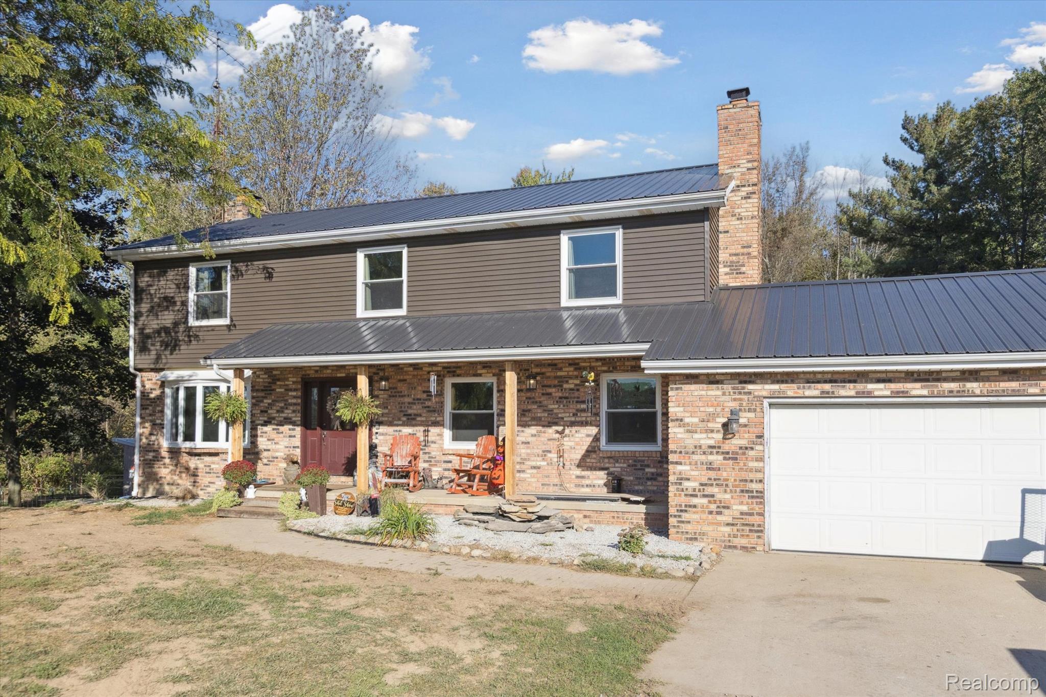 Traditional home featuring a porch, brick siding, a chimney, a metal roof, and a garage