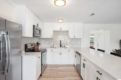 a kitchen with a sink dishwasher a refrigerator a stove and white cabinets with wooden floor