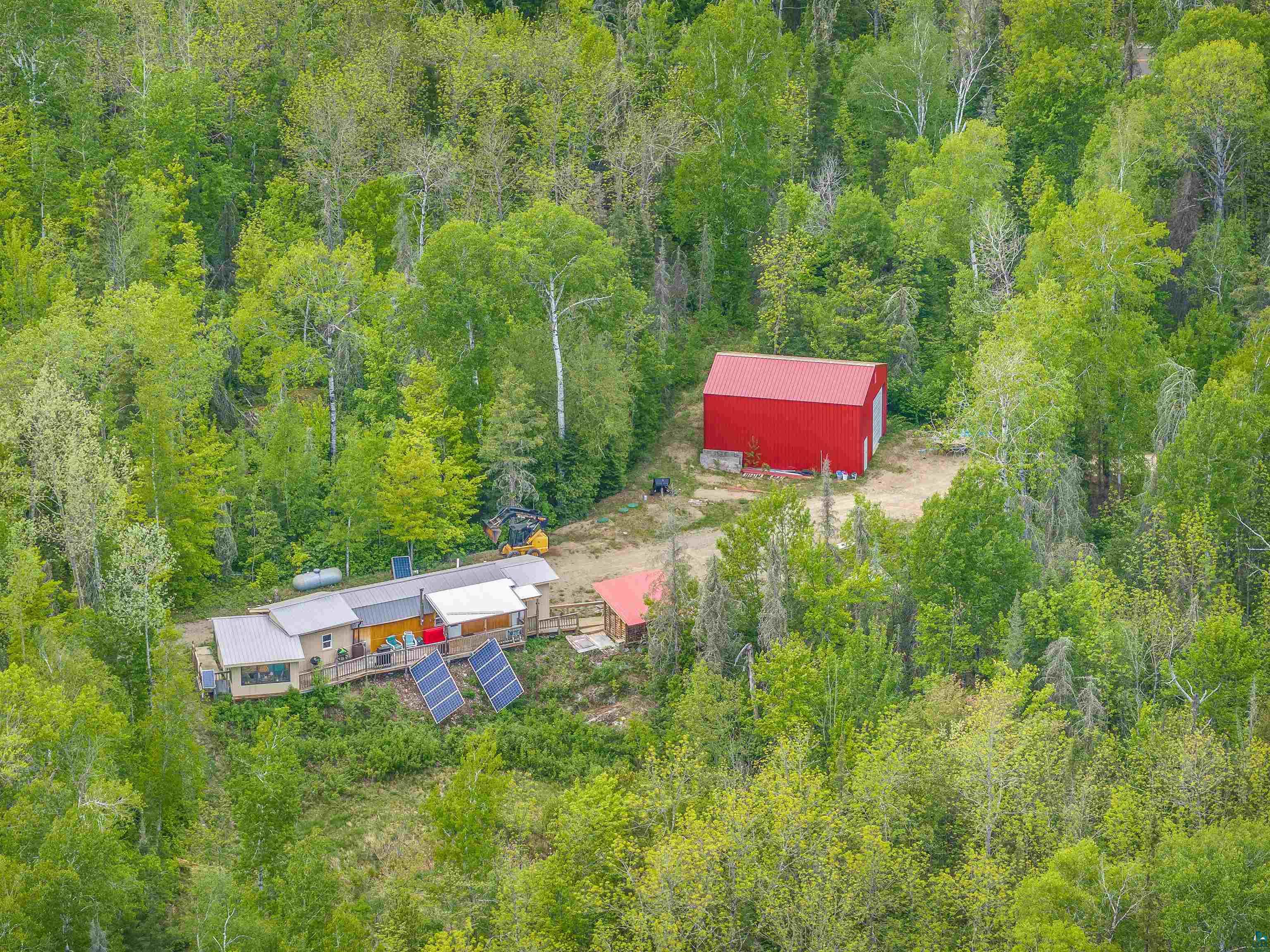 1152 Fernberg Road Ely, MN 55731 - Photo 12 of 24 Expansive wooded property featuring a primary residence with a long deck, multiple solar panel arrays, and a red auxiliary structure